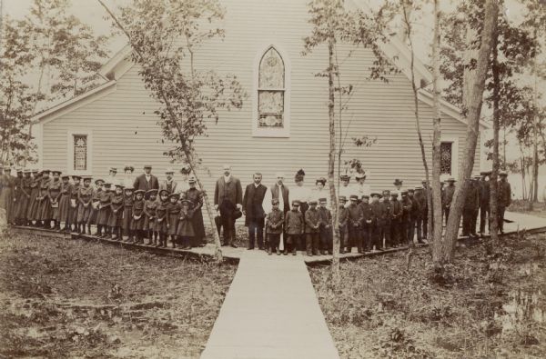 A group of children, teachers, and clergy in front of St. John's Mercer Memorial Chapel.