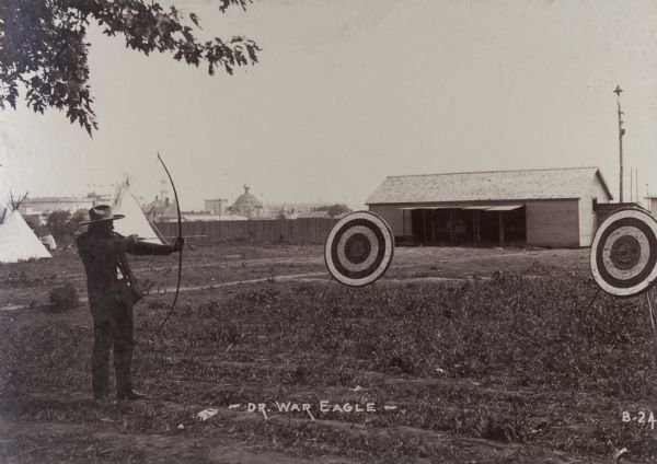 Dr. War Eagle shoots at a target using a bow and arrow at the Trans-Mississippi Exposition and Indian Congress.