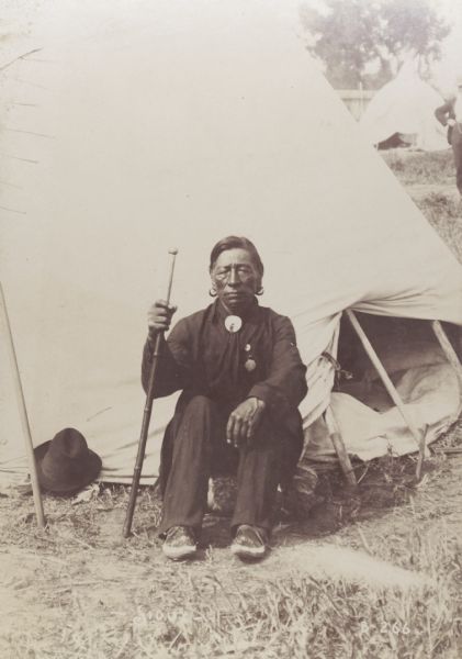 Withertail, a Sioux Chief, at the Trans-Mississippi Exposition and Indian Congress. He is sitting outdoors in front of a tipi.