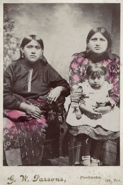 Studio portrait in front of a painted backdrop of two Osage women with an infant girl.