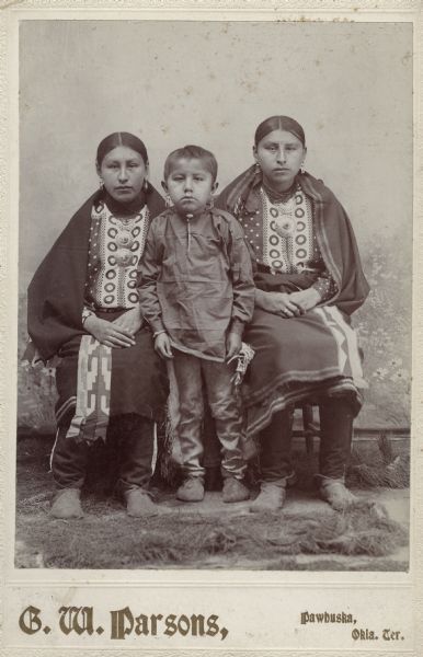 An Osage boy stands between two Osage women.