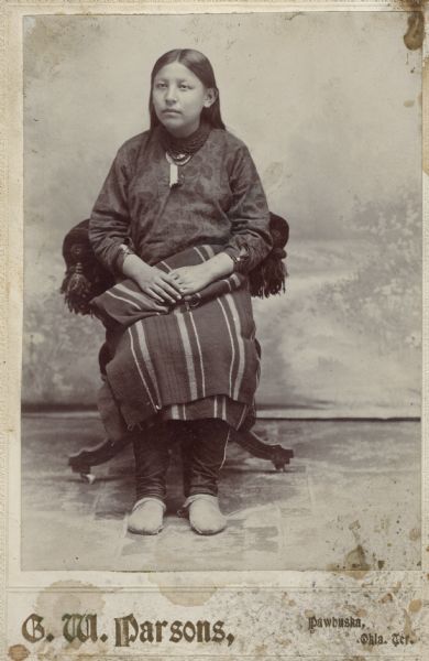 Studio portrait in front of a painted backdrop of an Osage woman sitting.