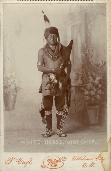 Full-length portrait of White Horse, an Otoe chief, posed in front of a painted backdrop.