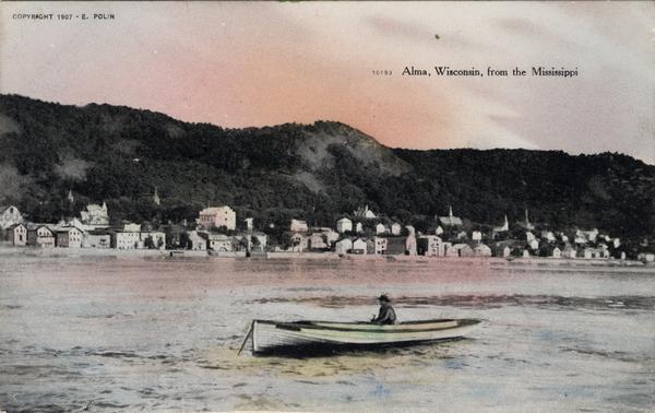View of Alma across the Mississippi River, with a man in a rowboat in the foreground. Caption reads: "Alma, Wisconsin, from the Mississippi."