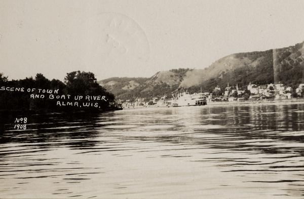 Caption reads: "Scene of Town and Boat Up River, Alma, Wis." View across river towards Alma on the opposite shoreline, and a river boat on the Mississippi River.