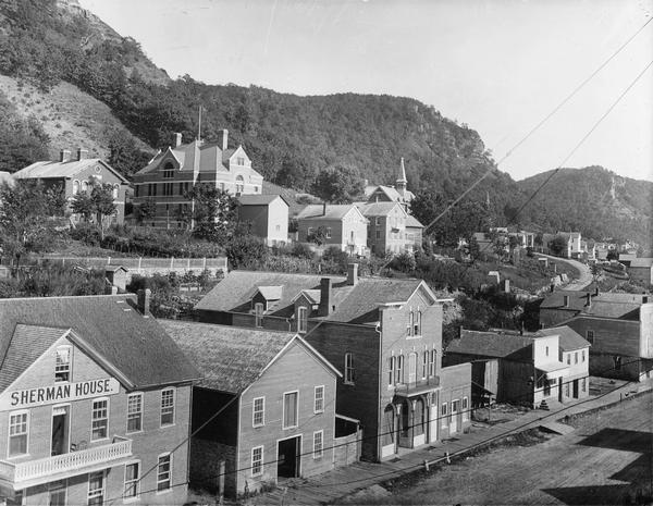 Elevated view of Alma. The Sherman House is in the left foreground. Houses are above and in the background are bluffs.