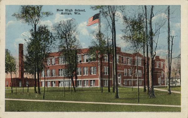 View across lawn with trees and sidewalks toward the high school. Caption reads: "New High School, Antigo, Wis."