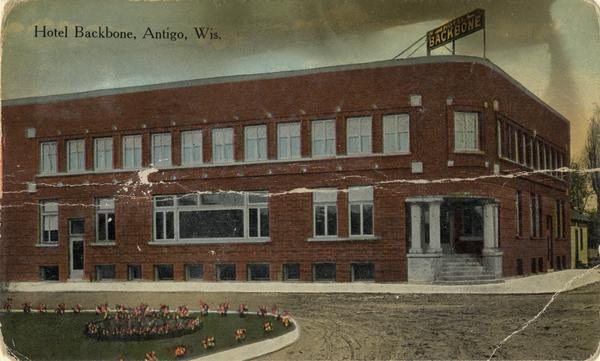 View toward the hotel on a street corner. A large sign on top of the hotel reads: "Hotel Backbone." Caption reads: "Hotel Backbone, Antigo, Wis."