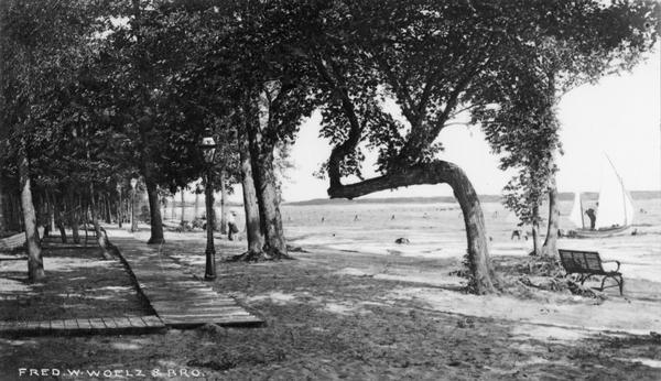 Aloah Beach on Lake Winnebago. There is a board sidewalk on the left. A sailboat is out on the lake on the right near the shoreline.