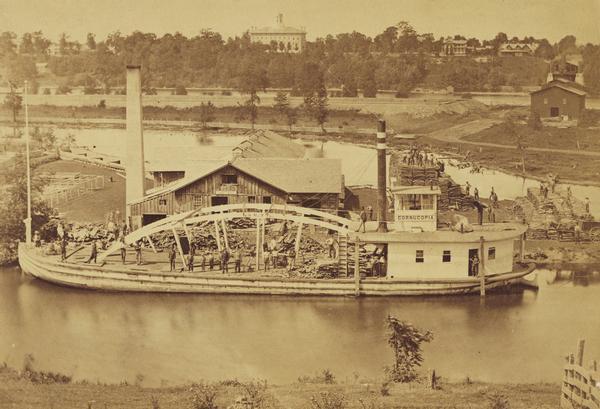 Elevated view from hill of the freight steamer "Cornucopia" loading hides at the Hammond Brothers warehouse, with Lawrence University buildings on the hill in the background. The "Cornucopia" was operated by Captain E.M. Neff.