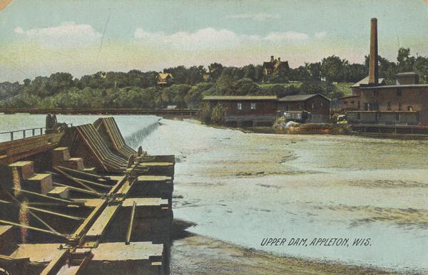 Upper dam on the Fox River. Industrial buildings are on the opposite shoreline, and large houses are among trees on the hill beyond. Caption reads: "Upper Dam, Appleton, Wis."