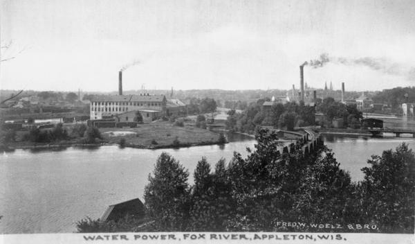 View of the power plant, along with a bridge, trees, and smokestacks.