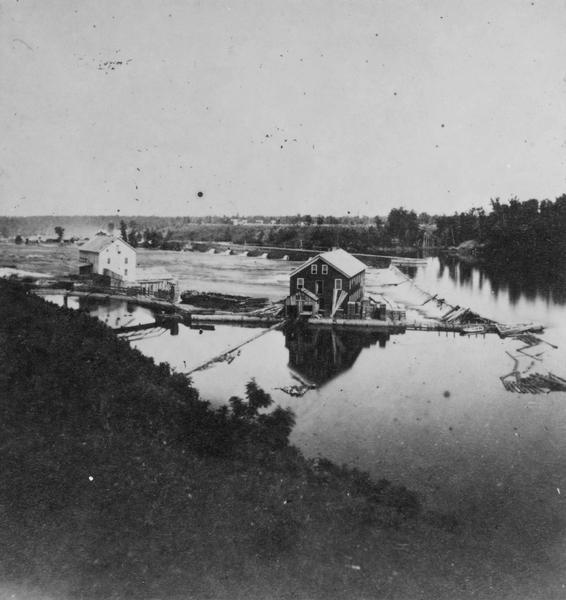 View from a hillside of either houses or factory buildings on the Fox River near a dam.