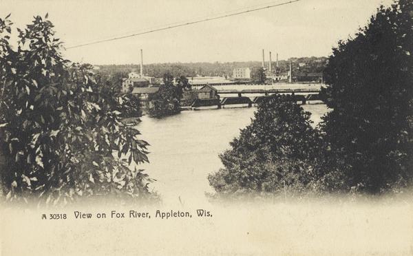 Elevated view from hill towards the Fox River and an industrial area through trees. A powerline is running across the skyline. Caption reads: "View on Fox River, Appleton, Wis."