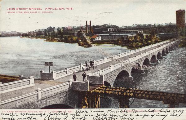 Elevated view of John Street Bridge. Caption reads: "John Street Bridge, Appleton, Wis. Largest stone arch bridge in Wisconsin." A railroad bridge runs across the bridge in the foreground.