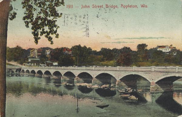 View from shoreline toward the bridge. Caption reads: "John Street Bridge, Appleton, Wis."