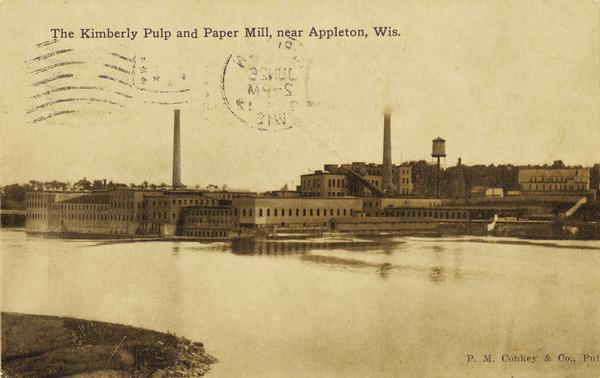 View from shoreline toward the mill on the opposite shoreline. Caption reads: "Kimberly Pulp and Paper Mill, near Appleton, Wis."