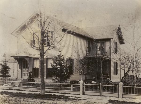 This is the H.W. Tenney house built by Charles Patten in the late 1870's, bought by Mr. Tenney in the spring of 1881. The people are, (left to right): Eva Edwards, Mrs. Tenney and Anna Tenney. It appears that Eva Edwards and Anna Tenney are on tricycles. The house was remodeled in 1906.