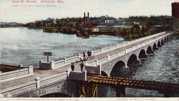 Elevated view of the bridge, which is intersected by a railroad bridge. Caption reads: "John St. Bridge, Appleton, Wis. Largest stone arch bridge in Wisconsin."