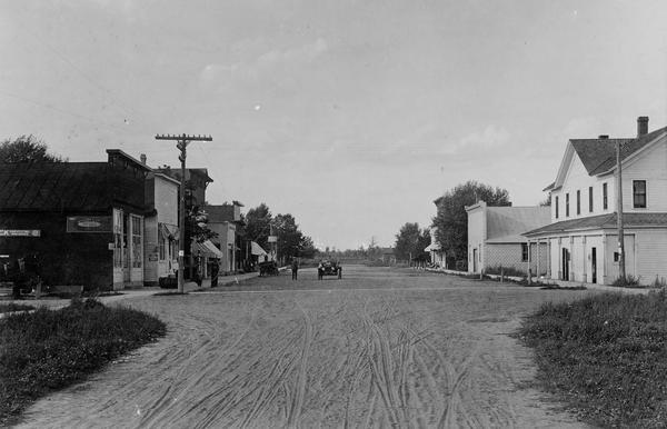 View down the unpaved main street of Argonne.  The inn in the right foreground was the Commercial House.  Across the street, the first building on the left was John Masbaum's store. An automobile and a pedestrian are in the street.