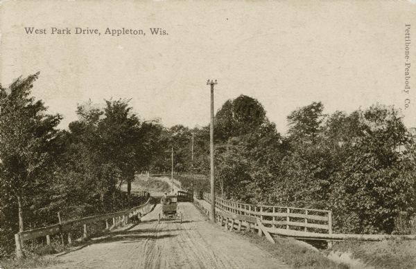 View down center of West Park Drive. There is a man driving an automobile on the bridge. Caption reads: "West Park Drive, Wis."