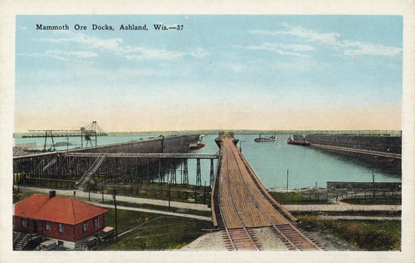 Caption reads: "Mammoth Ore Docks, Ashland, Wis." A building and roads are in the foreground. Several ore ships can be seen.