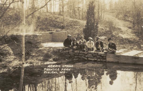 Six girls sit on a stone wall beside Mammoth Spring in Prentice Park.