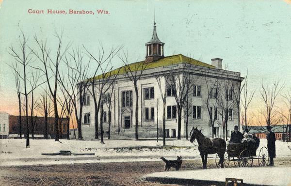 View towards a street corner. A dog and a man are standing in the street near a family sitting in a horse-drawn carriage. Snow is on the ground. Behind them is the Sauk County Court House. Caption reads: "Court House, Baraboo, Wis."