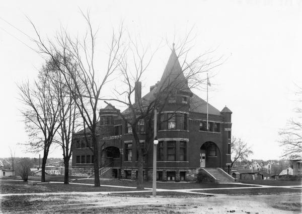 Dog kennels and houses border the Sauk County Jail in Baraboo. Taken from the Northeast corner of the intersection of Broadway and 2nd Avenue in Baraboo. The end of the building in the foreground is the Sheriff's family living quarters. The lower window in the facing turret was a dining area, the 2nd window was a parlor on main level, the 3rd window up was one of the bedrooms used by the family.