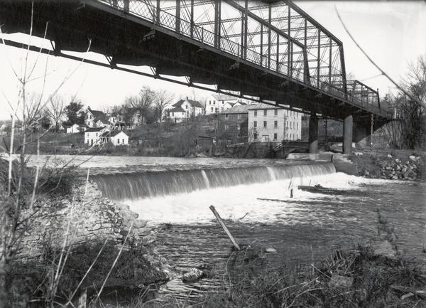 View of waterfall, bridge, Baraboo river, and town from the riverbank.