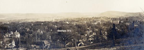Aerial view of town, with houses in foreground, and hills on the horizon in the background. Caption reads: "Baraboo, Wis."