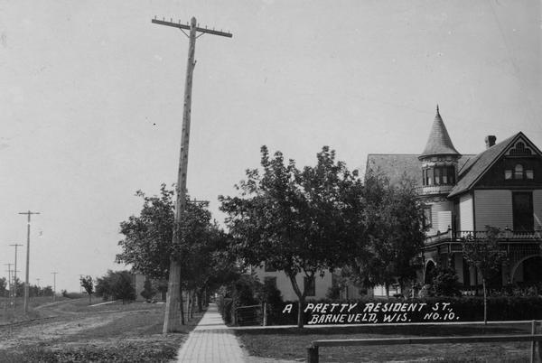 View down sidewalk in a residential street, with a house on the right. Caption reads: "A pretty Resident St., Barneveld, Wis."