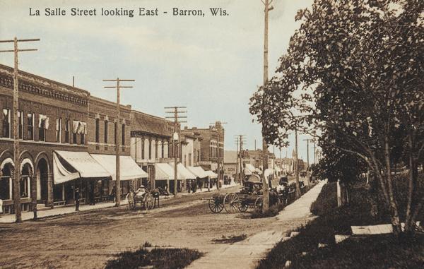 View of La Salle Street, looking east. Horse-drawn vehicles are along the right, and a person is driving a horse-drawn vehicle up the street on the left. Caption reads: "La Salle Street looking Easts — Barron, Wis."