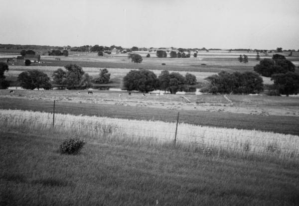 Field prior to the park's reconstruction, with a fence in the foreground. A river is at the bottom of the hill.