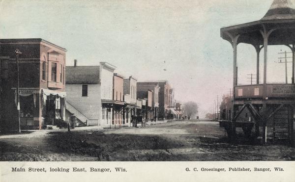 Caption reads: "Main Street, looking East, Bangor, Wis." View down Main Street with multiple two-storied businesses, and a pavilion on the street in the right foreground.