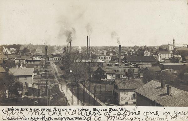 Caption reads: "Birds Eye View, from cotton mill tower, Beaver Dam, Wis." Two churches are in the background, and there are smokestacks and a water tower near industrial buildings.