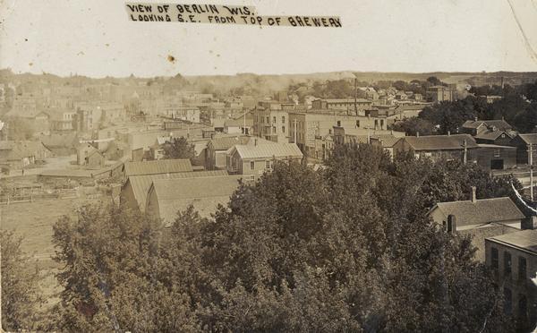View of the town, overlooking a grove of trees and a residential area and possibly Main Street. Caption reads: "View of Berlin Wis. Looking S.E. from Top of Brewery".