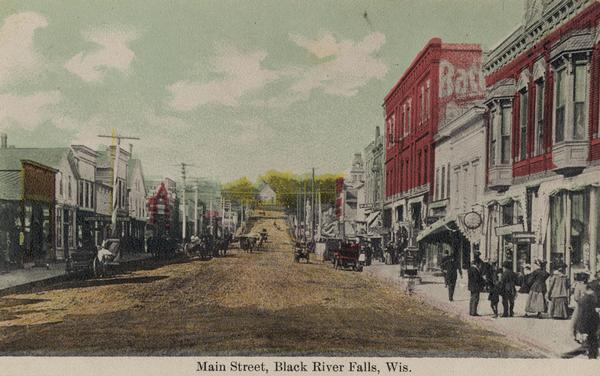 Caption reads: "Main Street, Black River Falls, Wis." View up Main Street, with people walking along the sidewalks, and automobiles parked along the curb.