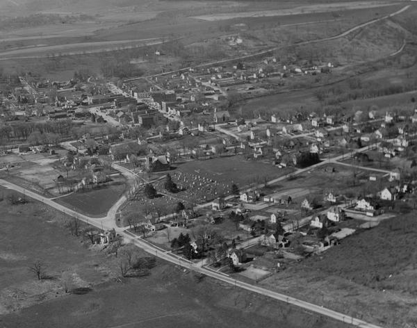 Air view of town, including multiple buildings and a cemetery.