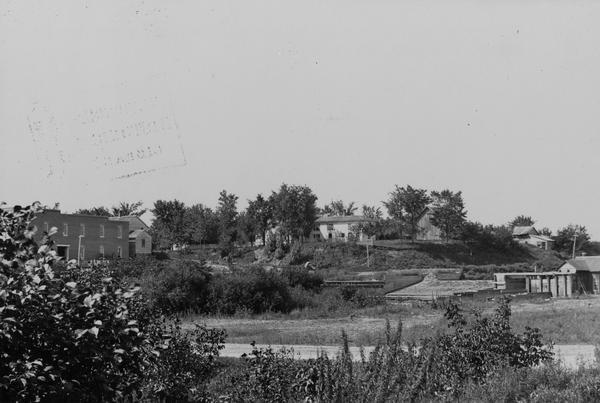 View from shoreline of Duncan Creek, with an old dam and on the oppostie shoreline, the residence of Fred Adler, the owner of a brewery and a store in the area.