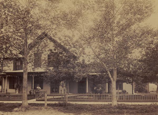 D.F. Brown house during the spring or summer, with two elm trees, three children and a woman. A picket fence runs along the sidewalk in the front of the house.