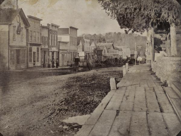 Canal Street less than a year before a fire swept through and destroyed many of these buildings on March 22, 1897, resulting in a loss of about $45,000. Primary focal point is the plank sidewalk on the right, with a clear view of many of the businesses on the left.