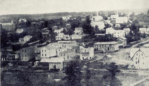 View of Bloomington by the pioneer photographer of the village, Frank Witcomb, sometime after 1873. There are buildings identified in the foreground on both the north and south sides of Canal Street. There are also building identifcations for Congress Street. Highlights include: The house at the corner of Canal and Congress was built by Ira Stockwell, the first village blacksmith, in 1852. Mr. Stockwell built his shop at the rear of his dwelling, on Congress Street. The Methodist, Baptist and Congregational churches, all built in the 1860's, are visible. Wm. Garner had his home on the west corner of Congress Street near the Rock School.