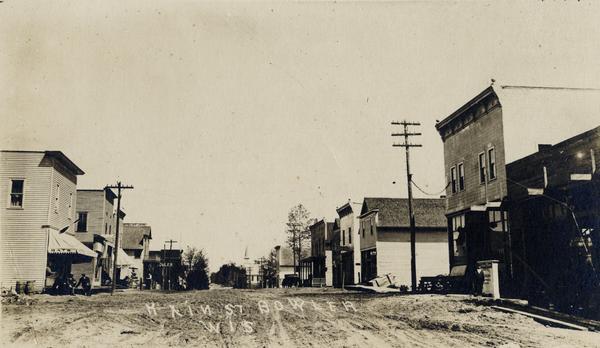 View down center of unpaved street. Caption reads: "Main St., Bowler Wis".