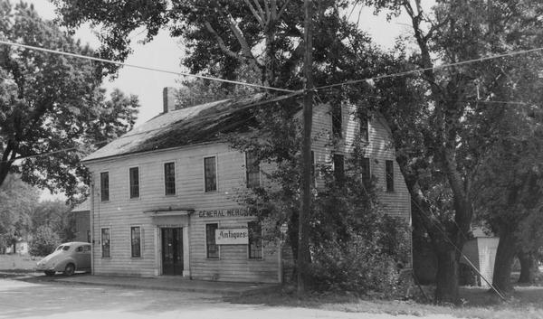 Image of the old general and antiques store.  Text reads: "House built as a store, allegedly by Augustin Grignon in 1848.  Later operated as a general store by Mr. Peterson and currently (1955) by Miss Emma Strauss."