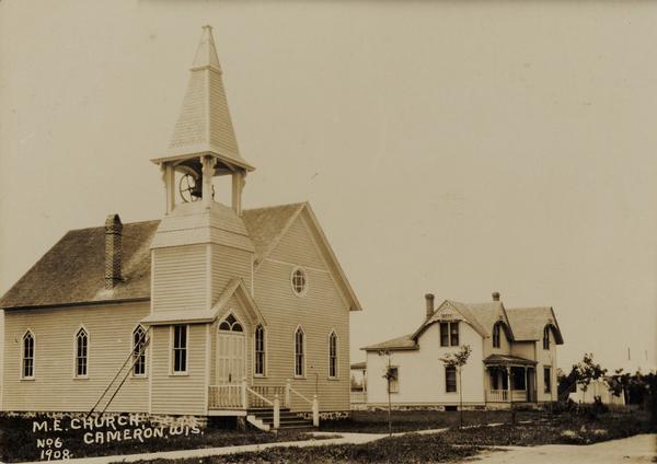 View of the Methodist Episcopal church. A ladder is set on the side of the belfry. A house is next to the church on the right.