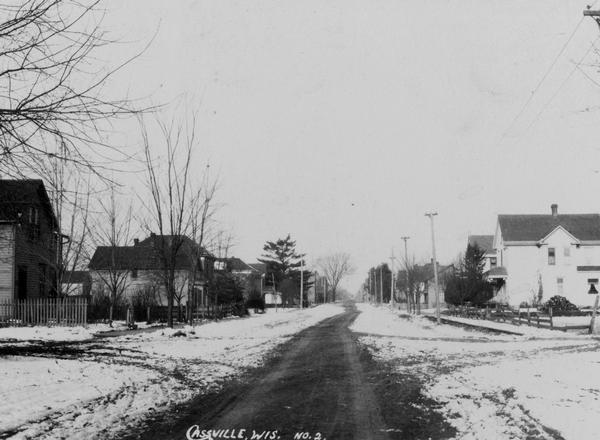 Snow-covered residential street with houses on each side.