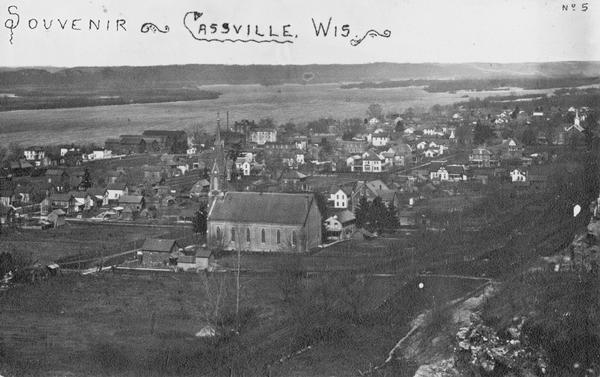 View from bluff looking northwest at the town of Cassville. A church in the center is the dominant structure in the foreground. Caption reads: "Souvenir - Cassville, Wis."