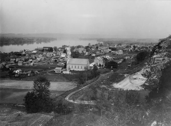 Cassville from the bluffs. Bluffs are in the right side of the image, and the view overlooks the town. The church is the dominant structure, and the river is in the background.
