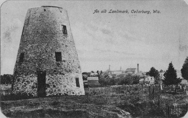 View of the stone building, with a town in the distance. Caption reads: "An old Landmark, Cedarburg, Wis."